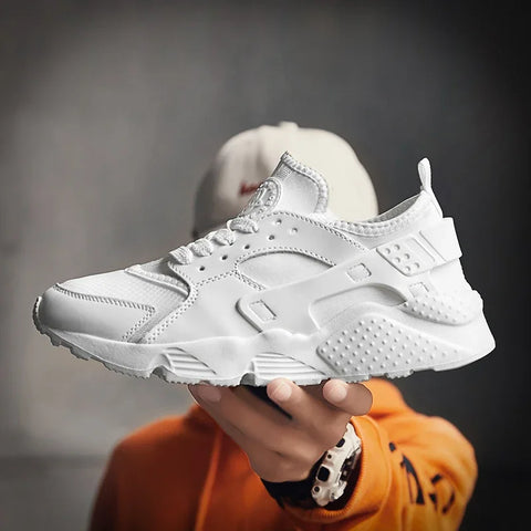 Beyaz Nike Air Huarache sneaker, Zolira unisex sneakers olarak bir el ile tutuluyor